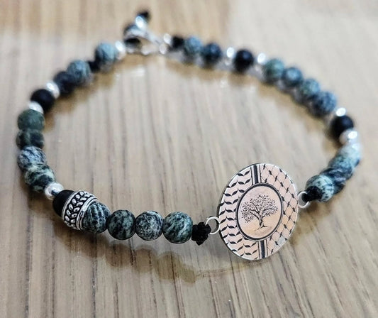 Bracelet with green beads and a circular tree design charm on a wooden surface