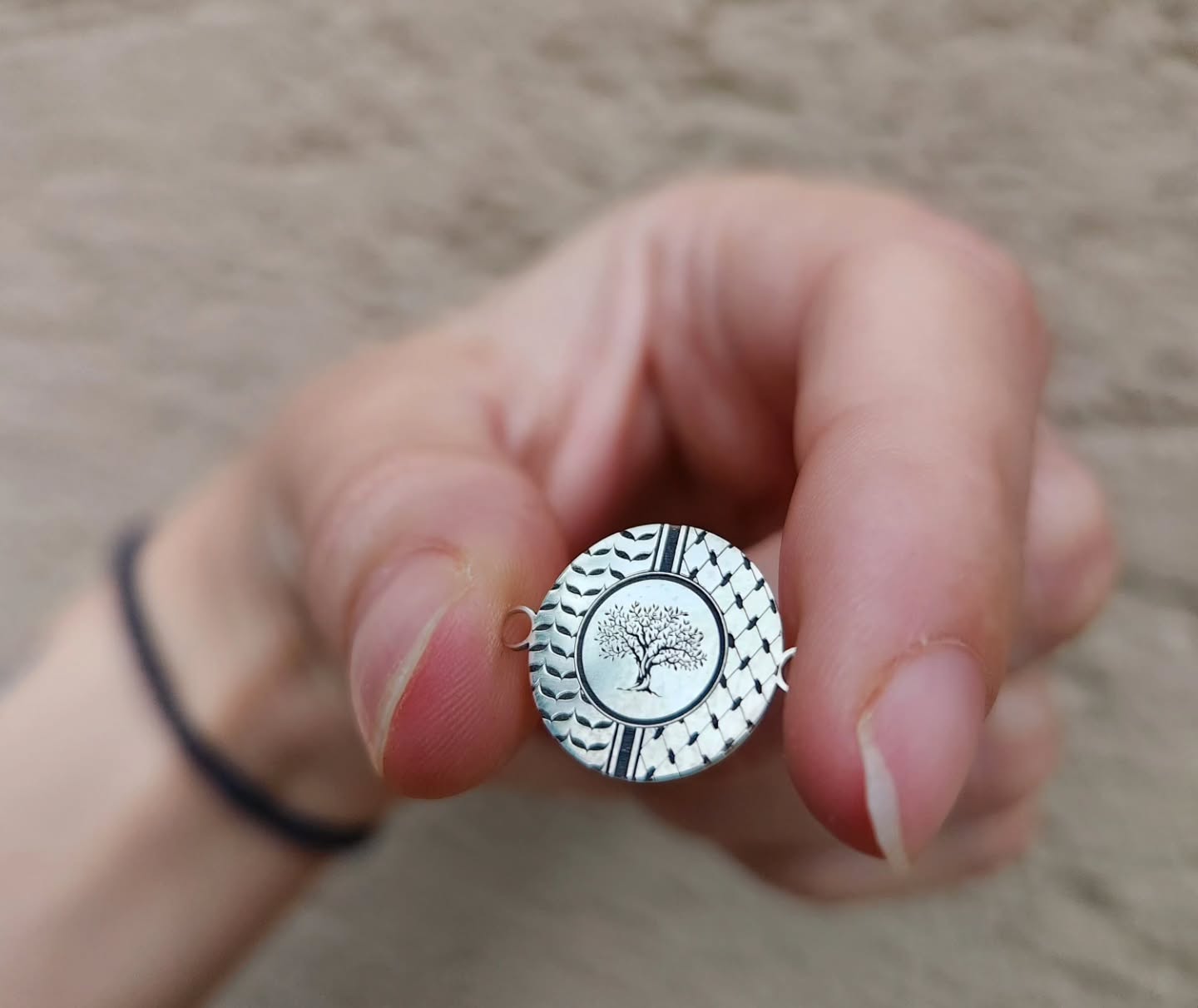Hand holding a silver locket with a tree design against a neutral background