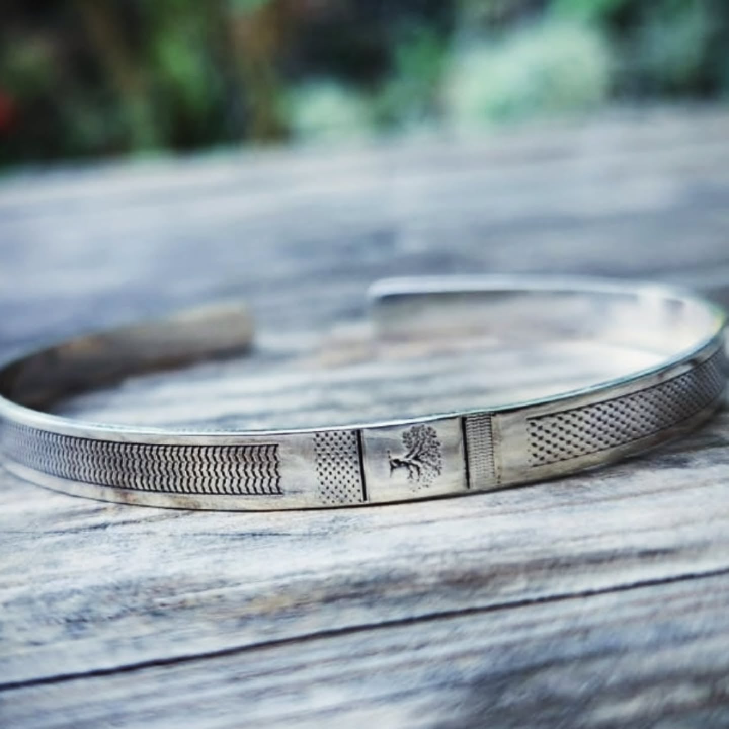 Silver bracelet with engraved patterns on a wooden surface
