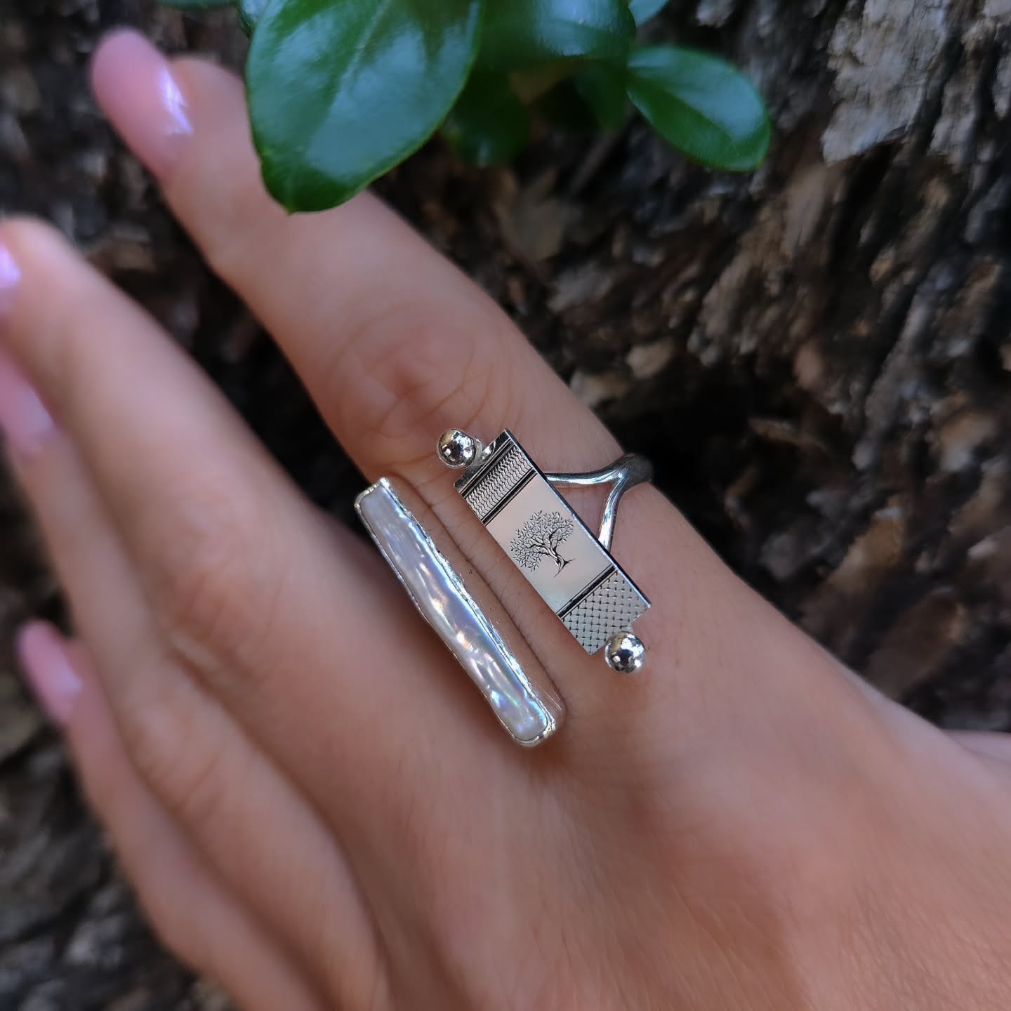 Hand wearing a silver ring with a tree design and pearls, against a natural background.