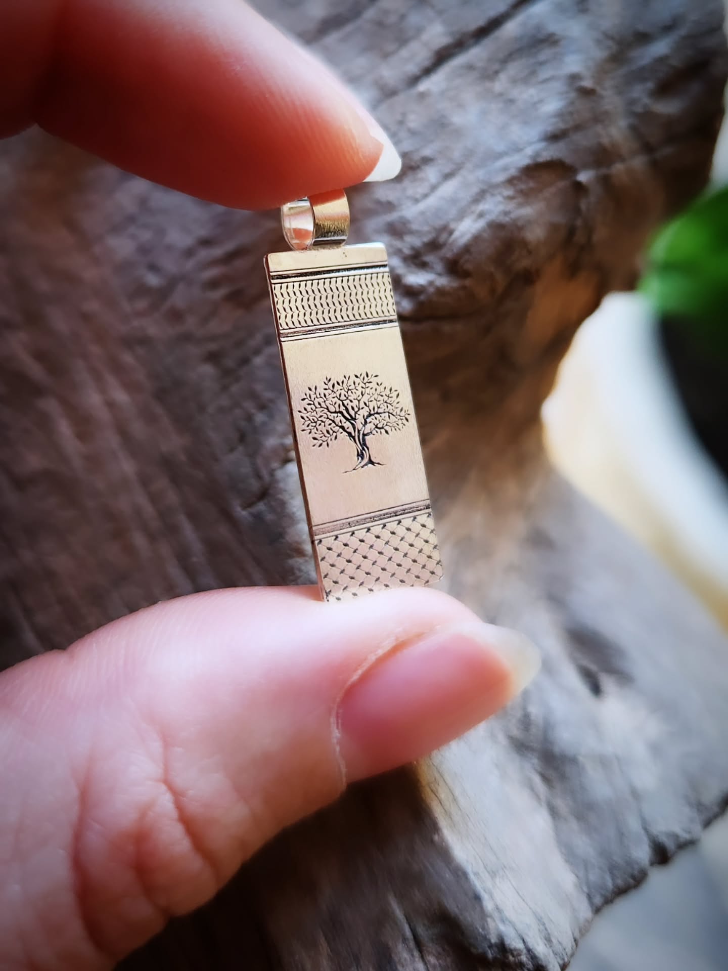 Silver pendant with tree design held by a hand against a wooden background