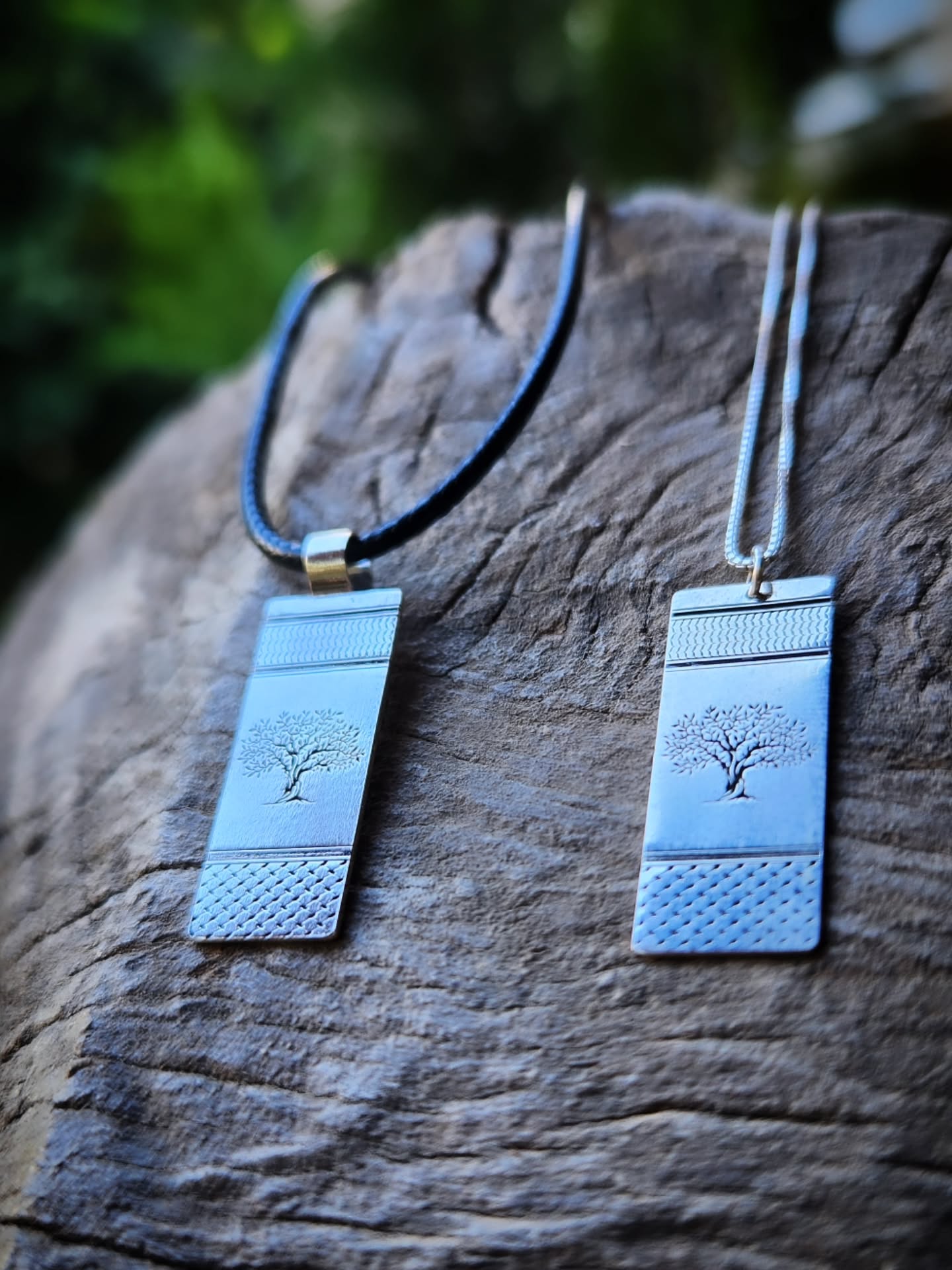 Two necklaces with tree designs on rectangular pendants hanging on a wooden surface.