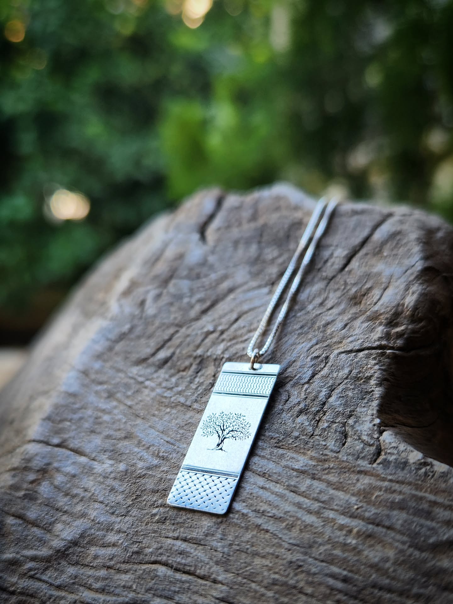 Silver pendant necklace on a wooden surface with a blurred green background