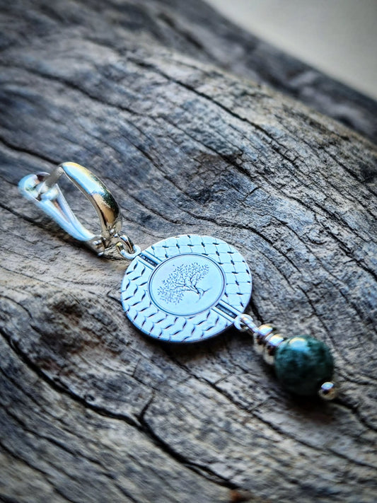 Pair of earrings with circular  tree design and a green bead on a wooden background