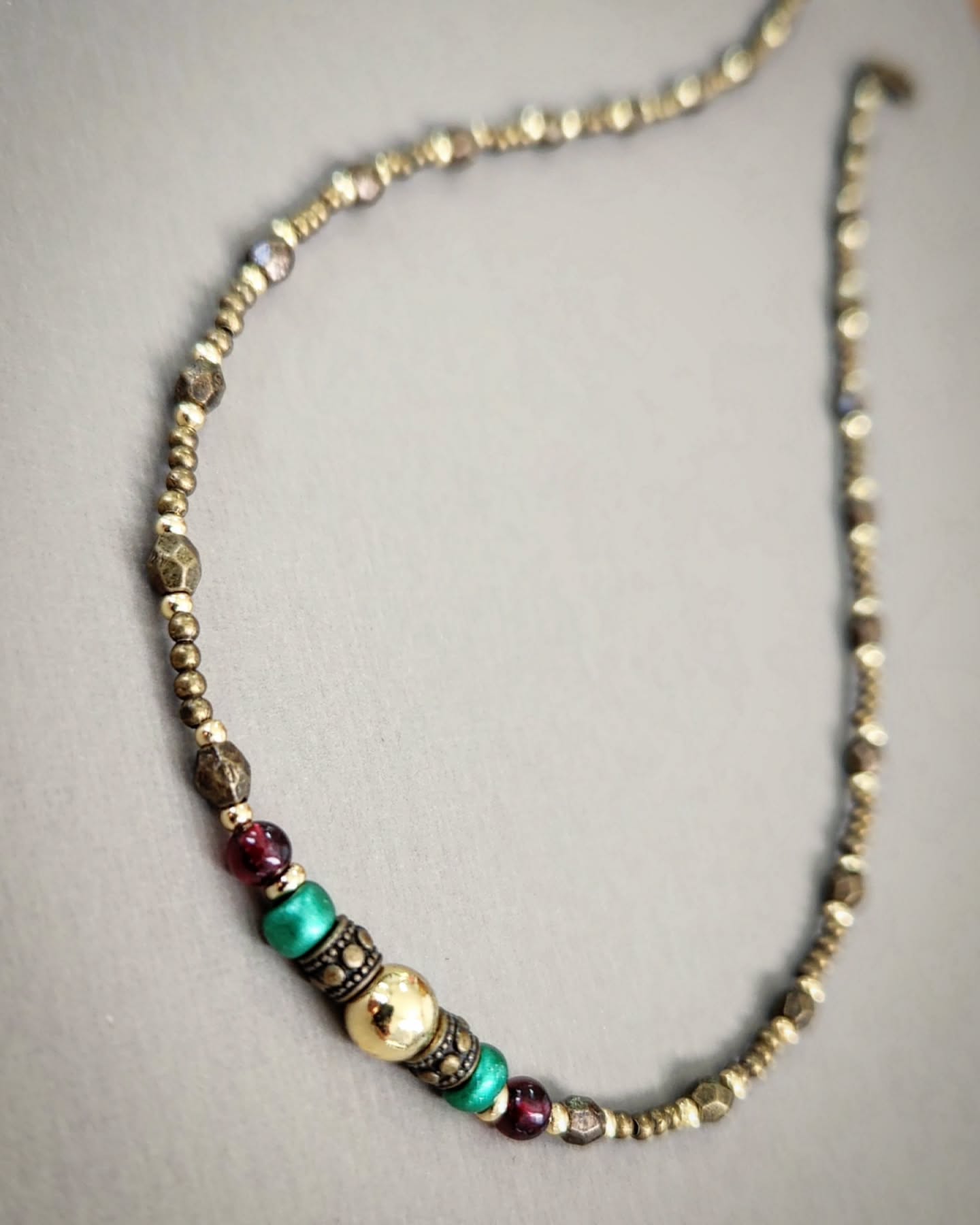Bronze necklace with gold, red and turquoise beads on a gray background