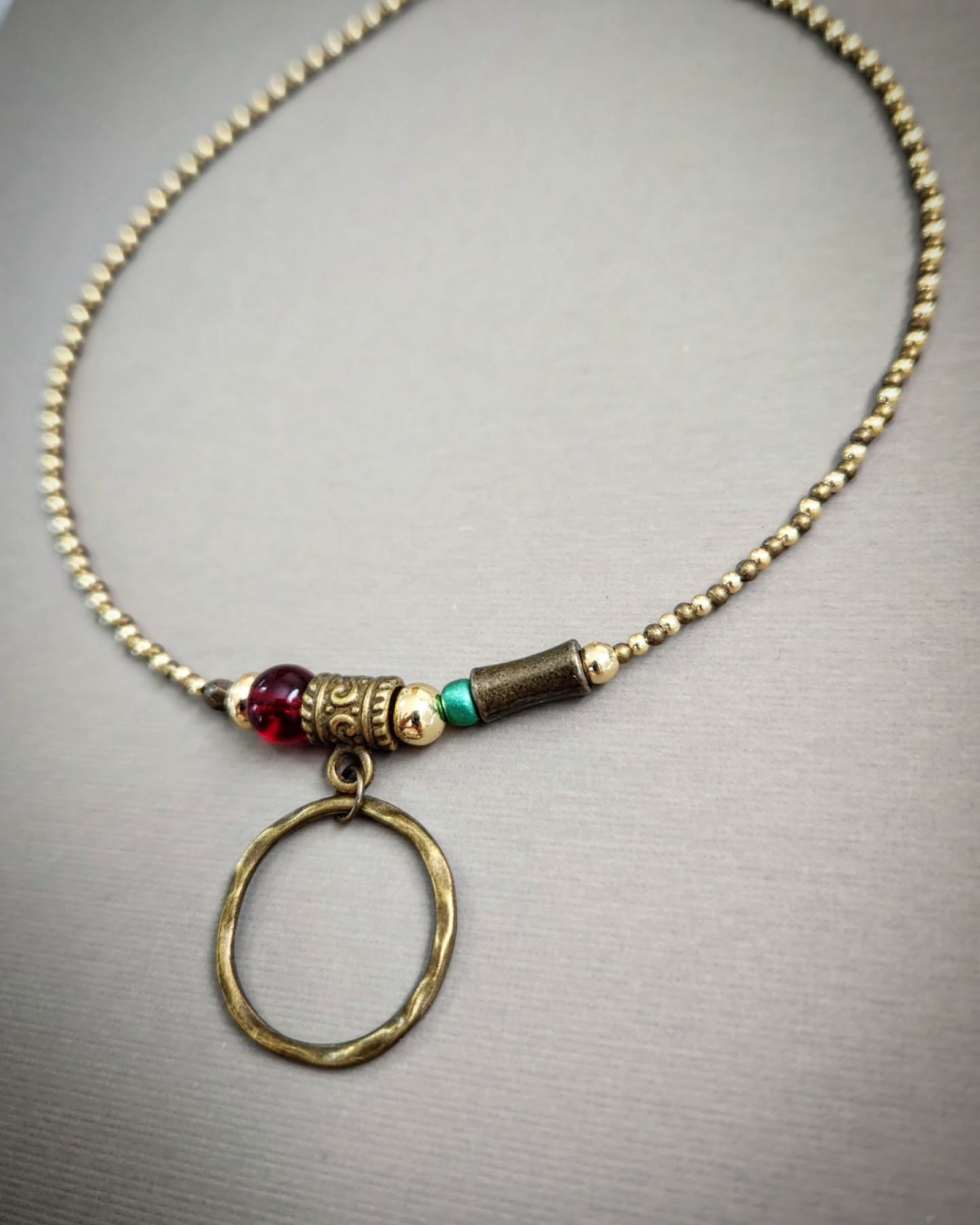 Bronze necklace with gold, red and turquoise beads on a gray background