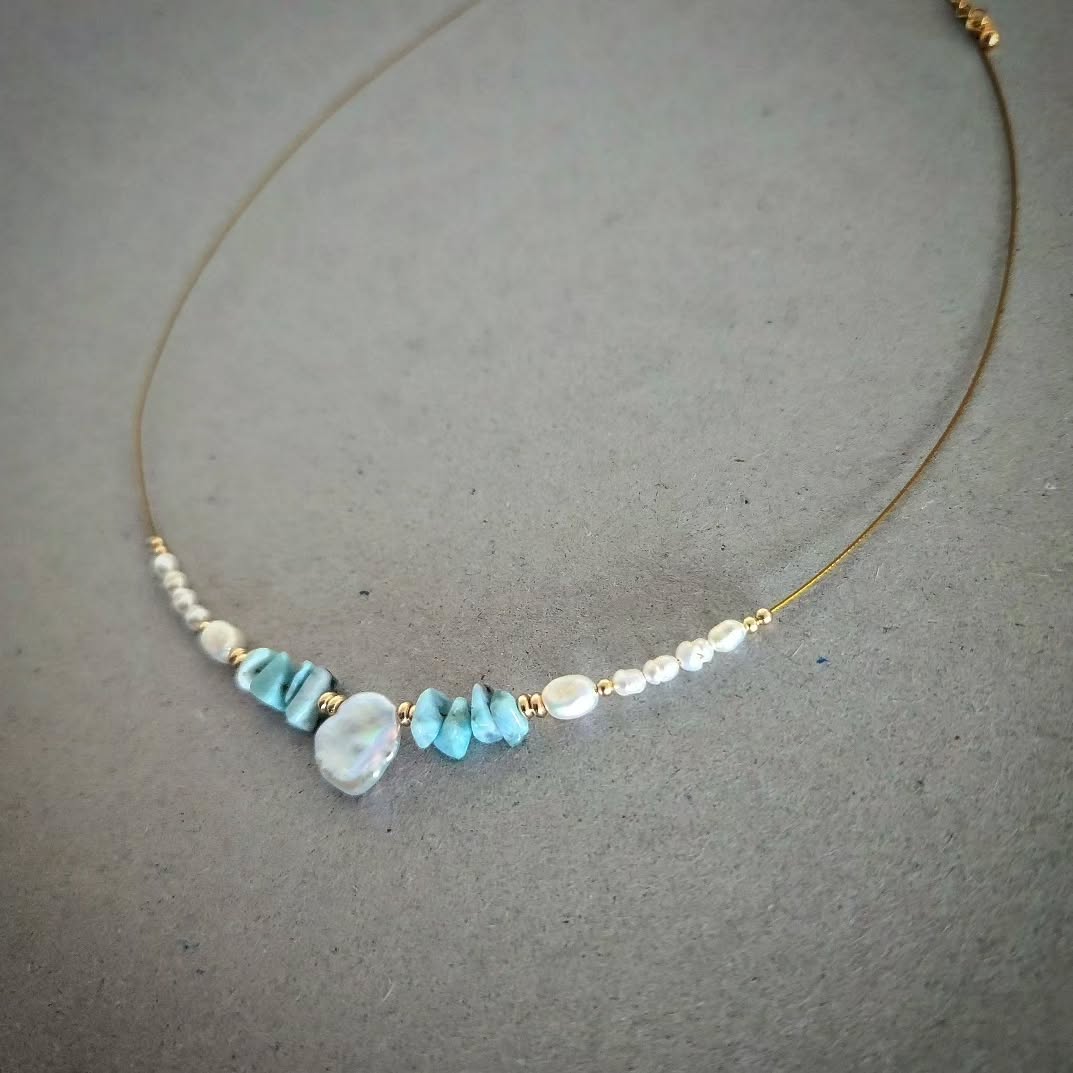 Gold plated necklace with turquoise and pearl beads on a gray background
