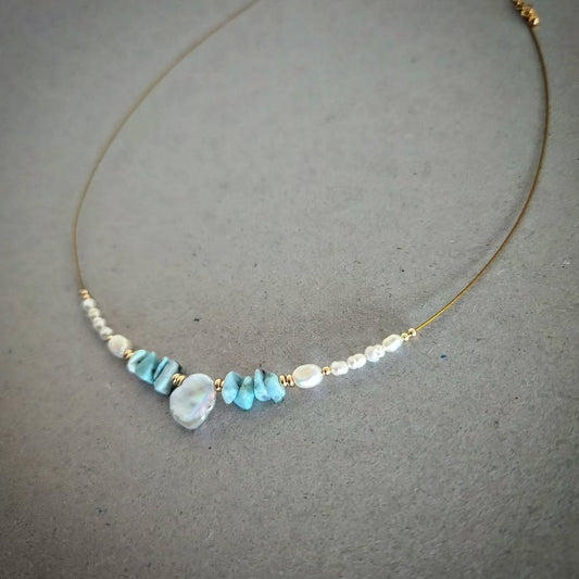 Gold plated necklace with turquoise and pearl beads on a gray background