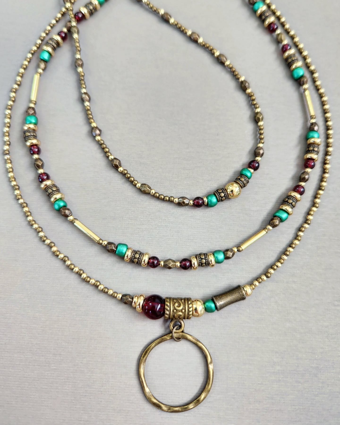 Three layered bronze necklaces with gold, red and turquoise beads on a gray background