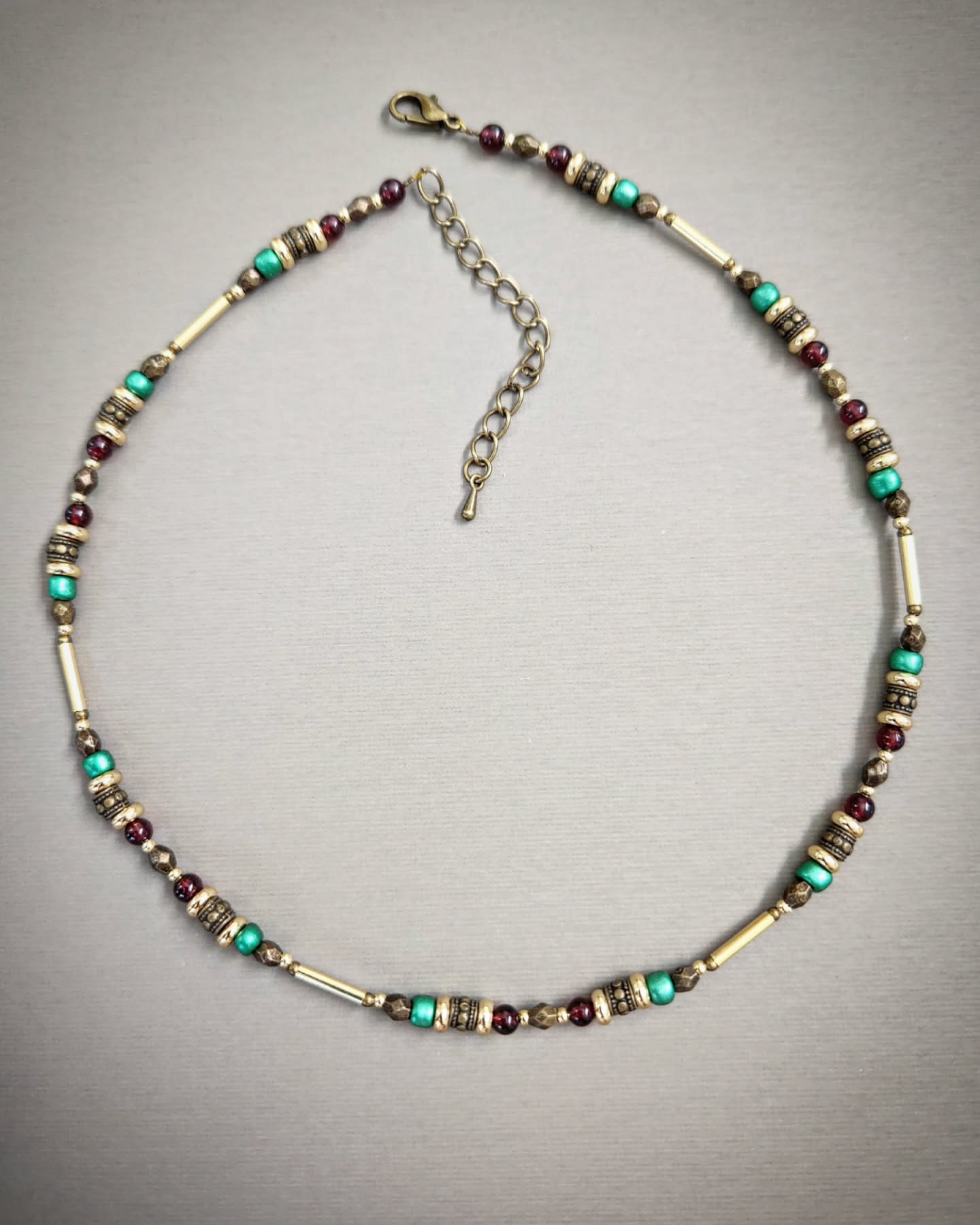 Bronze necklace with gold, red and turquoise beads on a gray background
