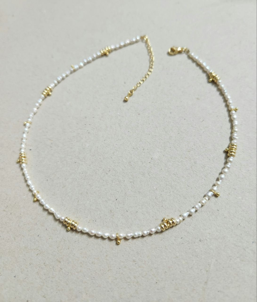 Necklace with pearl beads and gold accents on a light gray background