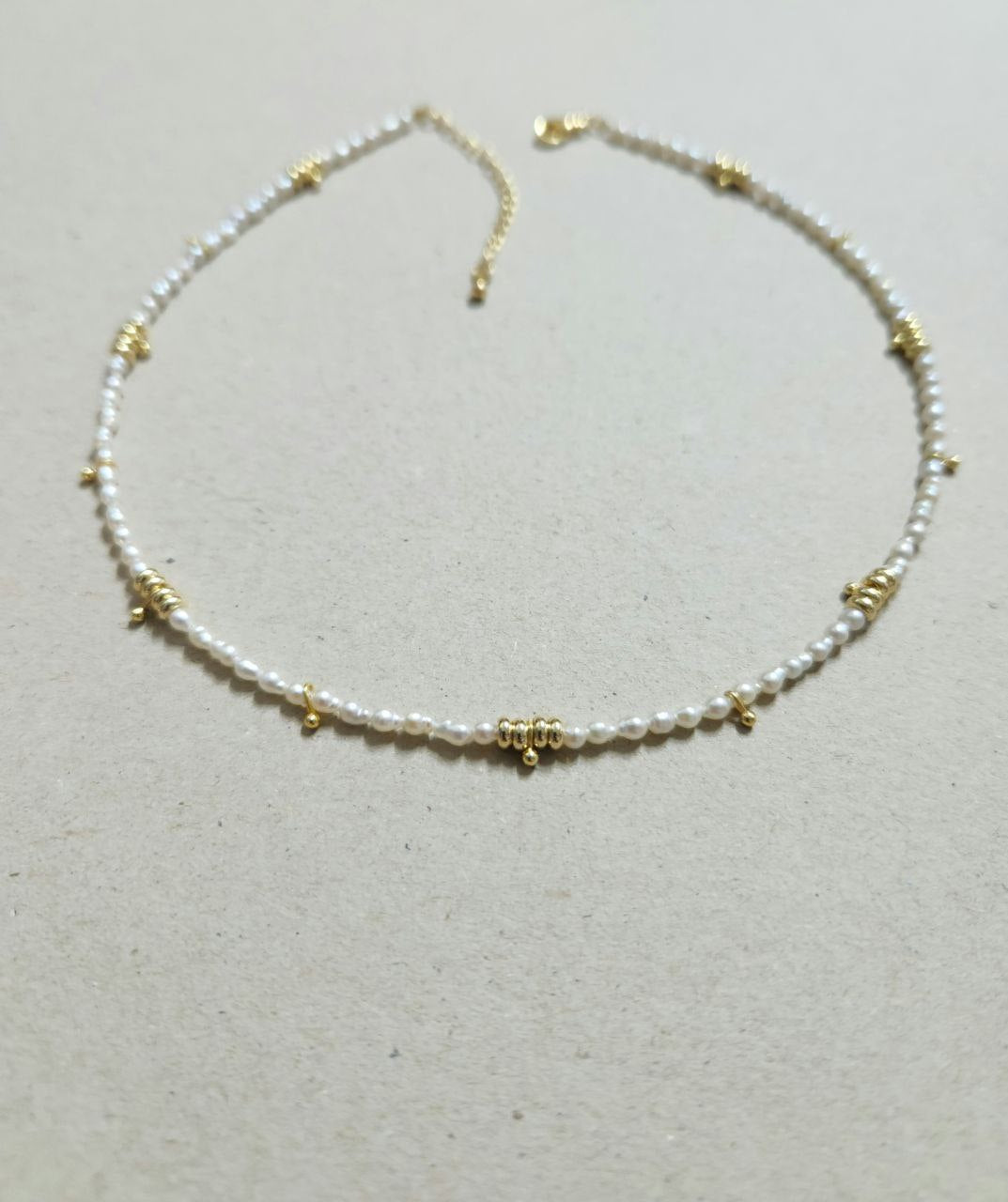 Necklace with pearl beads and gold accents on a light gray background