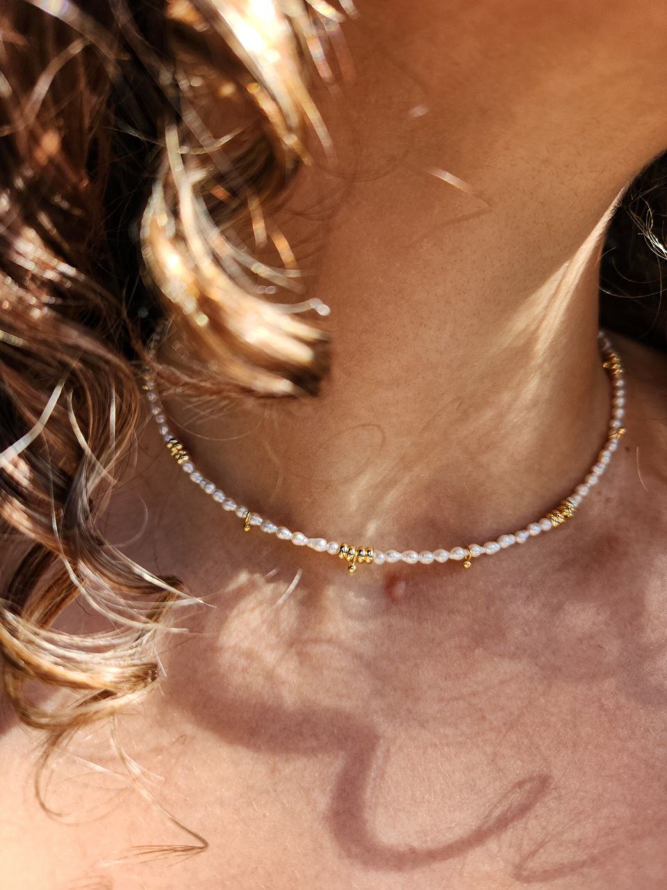 Close-up of a person wearing a necklace with pearl beads and gold accents on a light gray background