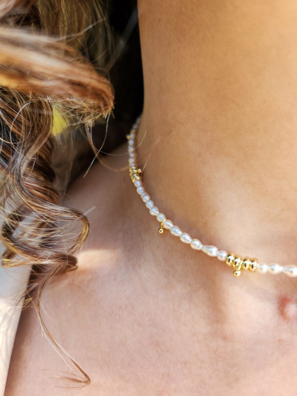 Close-up of a person wearing a necklace with pearl beads and gold accents on a light gray background