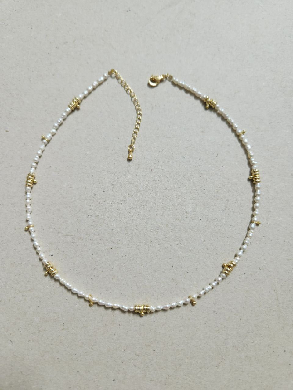 Necklace with pearl beads and gold accents on a light gray background