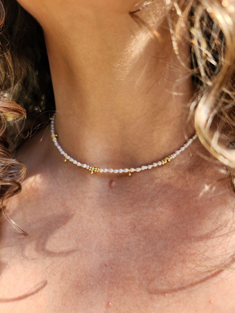 Close-up of a person wearing a necklace with pearl beads and gold accents on a light gray background